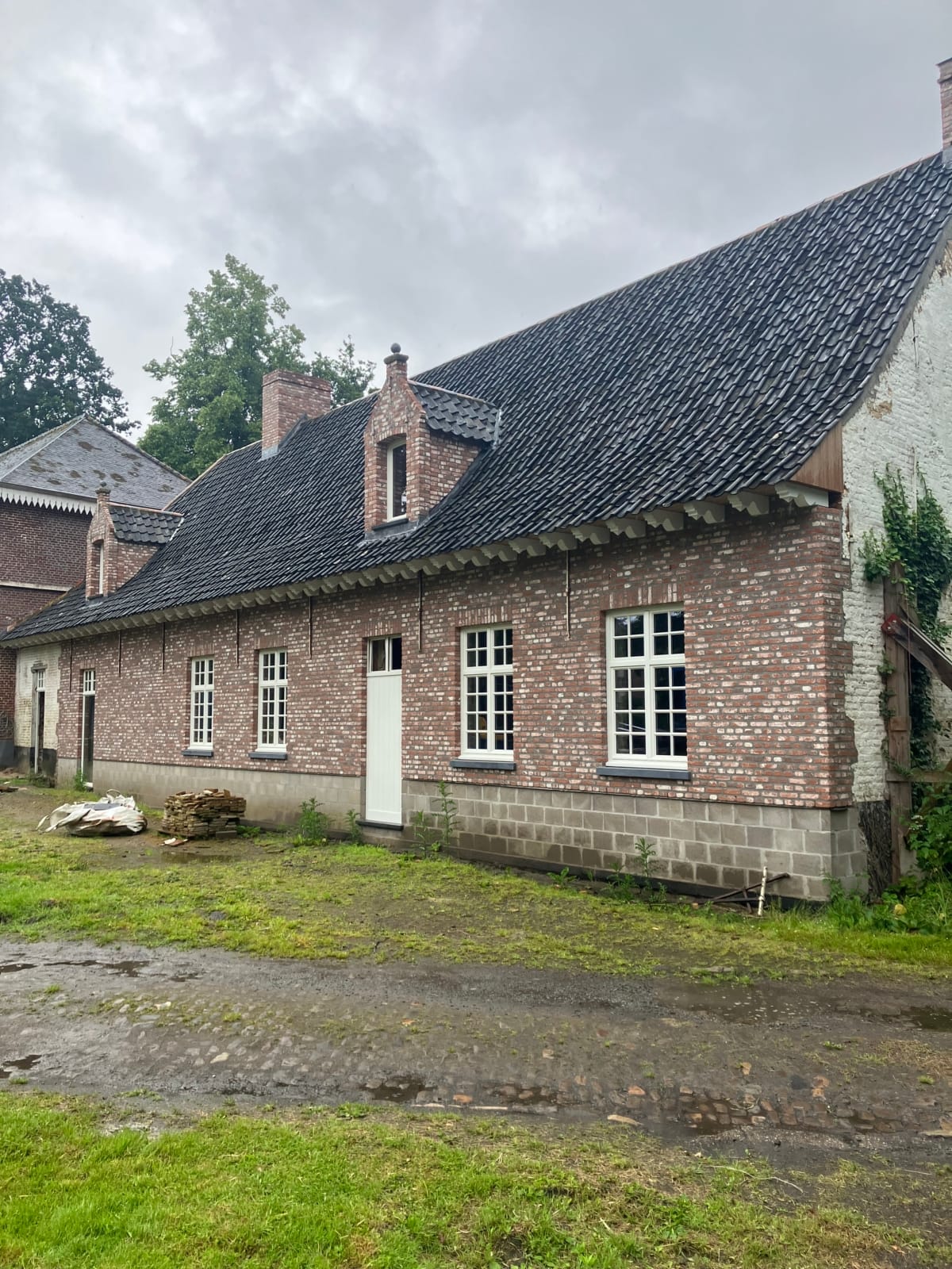 Verbouwde woning in De Pinte met een gevel in rode baksteen, witte ramen met kleine ruiten en een steil dak met twee dakkapellen, een project van Bouwwerken Goossens