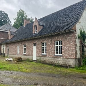 Verbouwde woning in De Pinte met een gevel in rode baksteen, witte ramen met kleine ruiten en een steil dak met twee dakkapellen, een project van Bouwwerken Goossens
