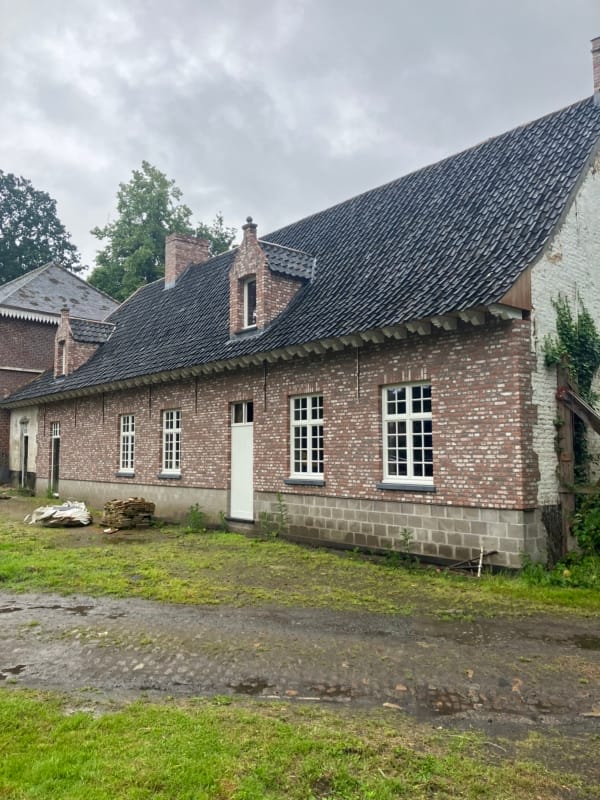 Verbouwde woning in De Pinte met een gevel in rode baksteen, witte ramen met kleine ruiten en een steil dak met twee dakkapellen, een project van Bouwwerken Goossens