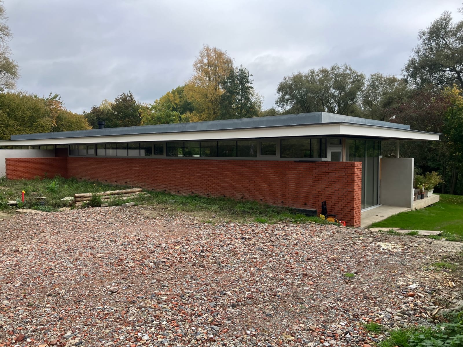 Lange zijgevel van de nieuwbouwwoning in Deux-Acren, met rode baksteen onderaan en een strook ramen onder de witte dakrand, een project van Bouwwerken Goossens