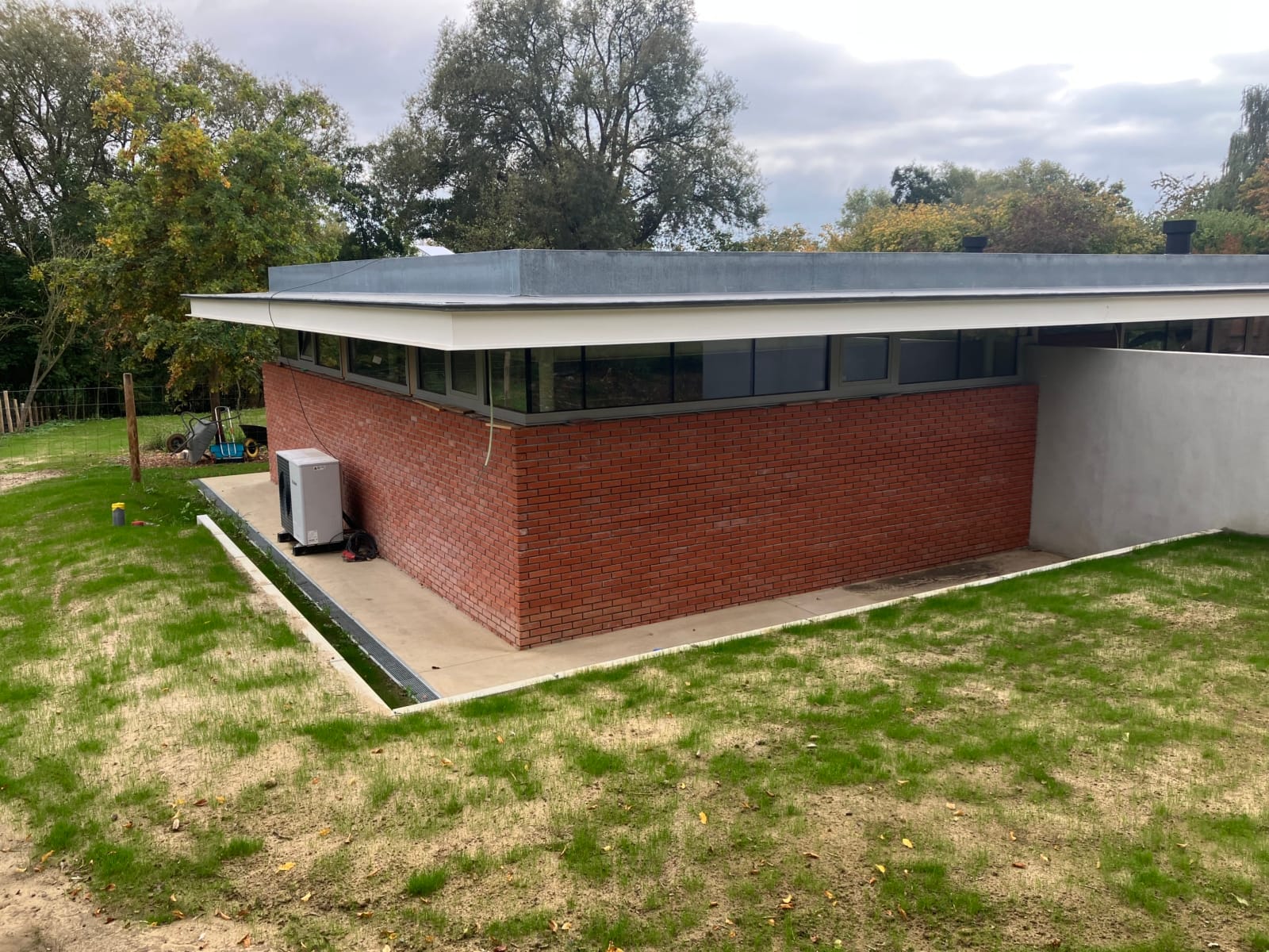 Hoek van de nieuwbouwwoning in Deux-Acren met een gevel in rode baksteen, een strook ramen en een plat dak met ver uitstekende dakrand, een project van Bouwwerken Goossens