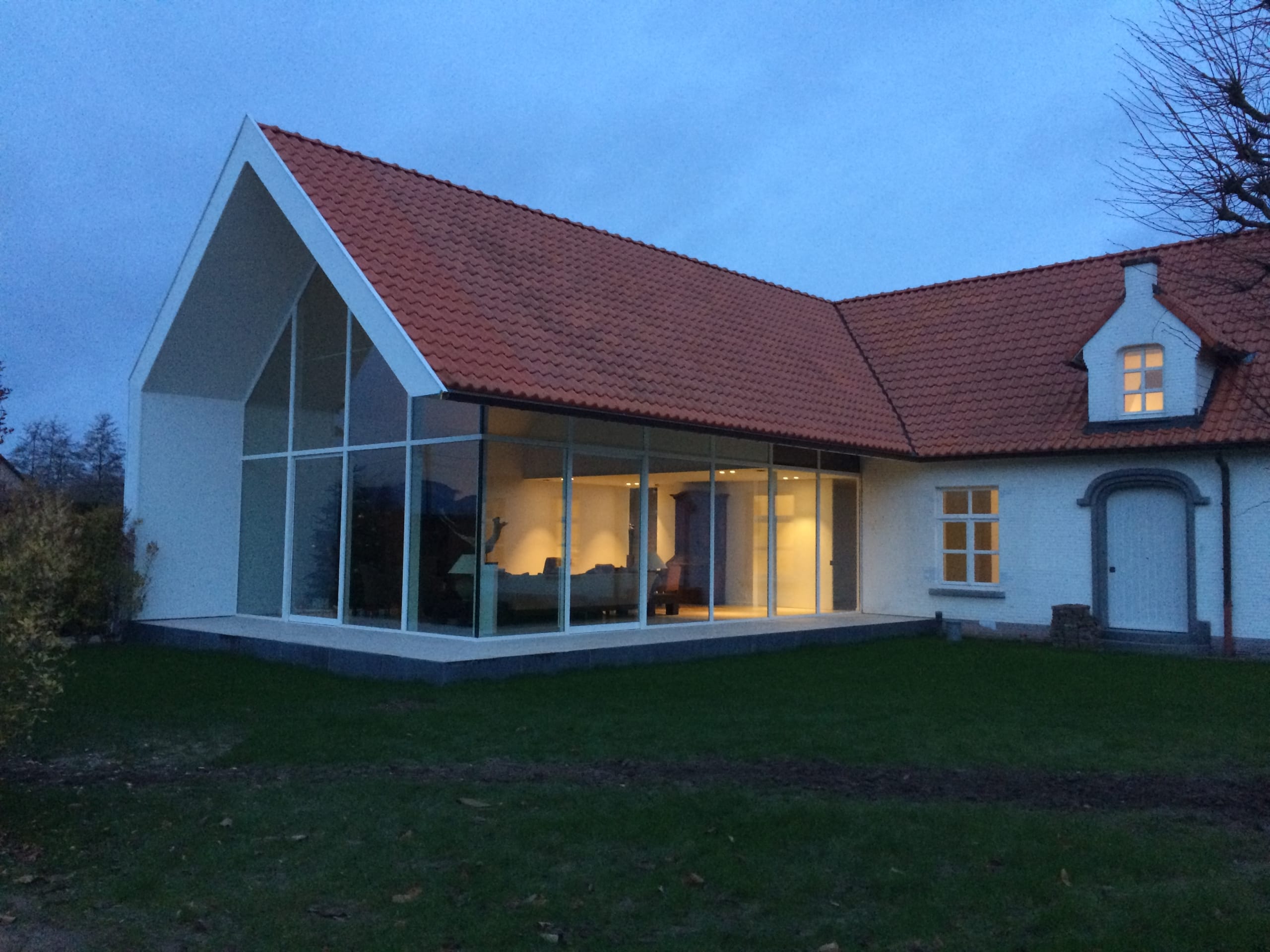 Glazen aanbouw met rood pannendak dat aansluit op het dak van de hoeve