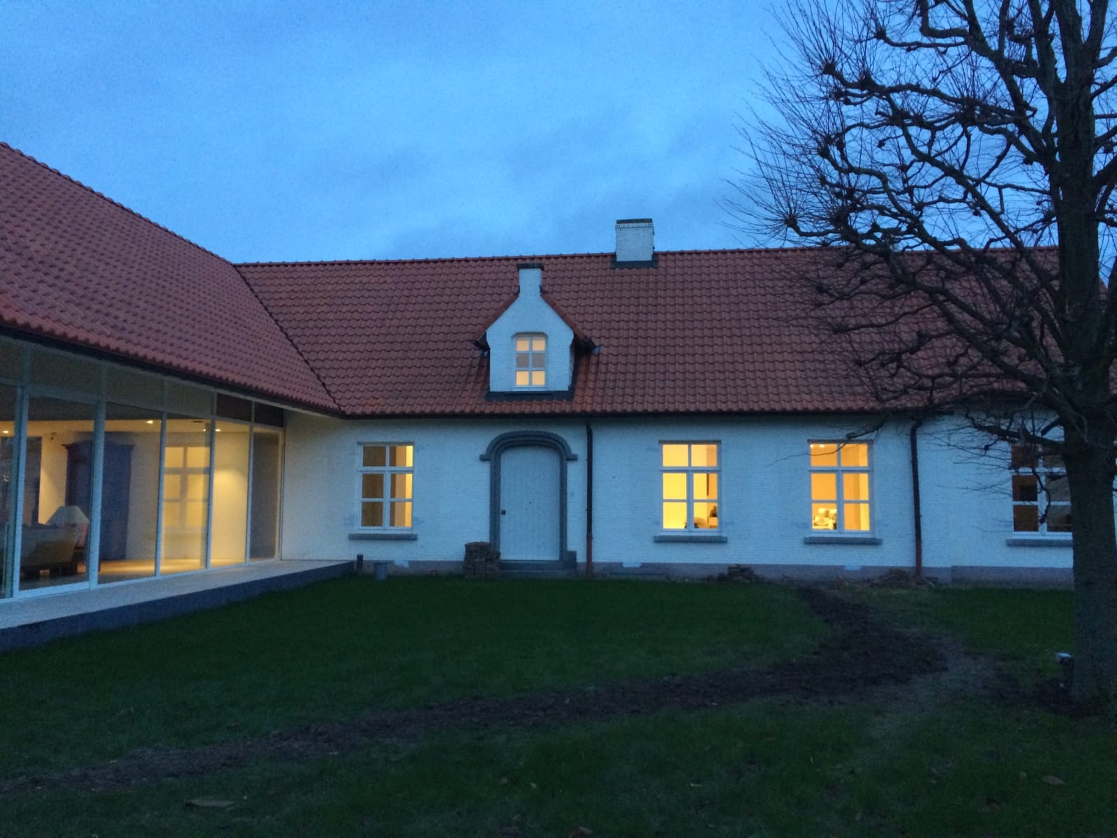 Gevel van de bestaande hoeve met dakkapel, links de glazen wanden van de nieuwe aanbouw