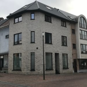 Verbouwd hoekpand in Brakel met drie bouwlagen, een gevel in lichtgrijze gevelsteen en donkere ramen, een project van Bouwwerken Goossens