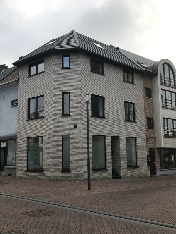 Verbouwd hoekpand in Brakel met drie bouwlagen, een gevel in lichtgrijze gevelsteen en donkere ramen, een project van Bouwwerken Goossens