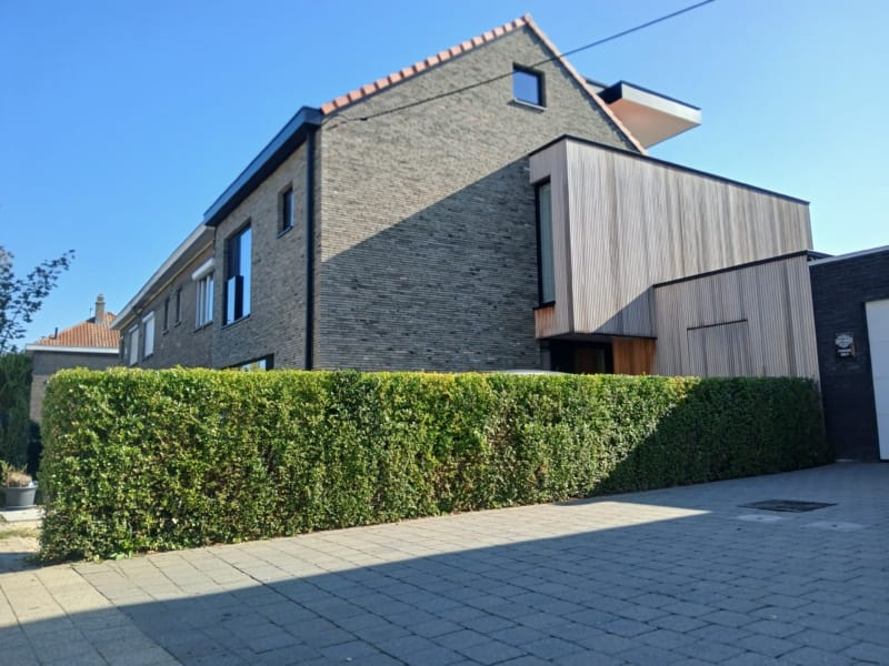 Verbouwde halfopen woning in Gentbrugge met een gevel in donkere baksteen, een uitbouw met verticale houten latten en een rood pannendak, een project van Bouwwerken Goossens