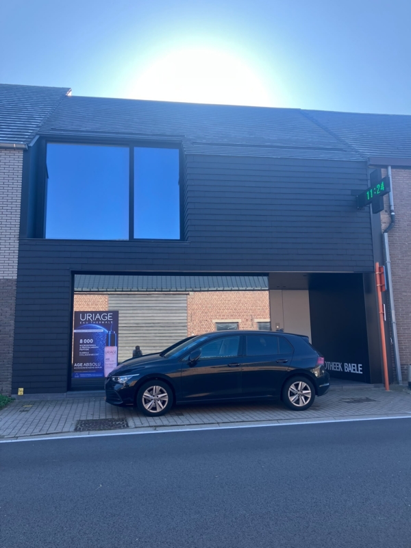Nieuwe apotheek in Bavegem met een zwarte voorgevel in leien, een groot raam op de verdieping en een groot raam op het gelijkvloers, een project van Bouwwerken Goossens