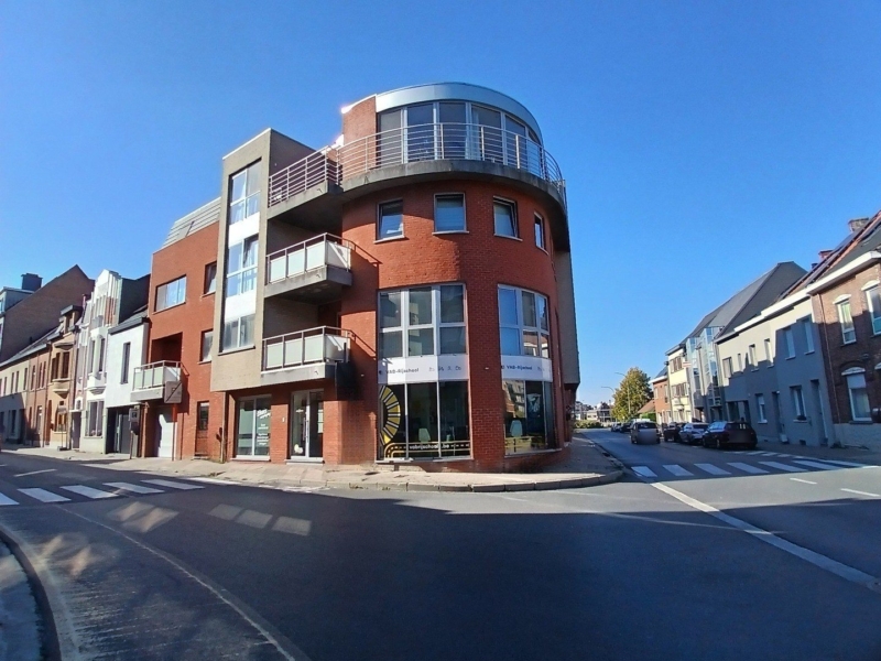 Nieuw appartementsgebouw op een hoek in Zottegem met een ronde gevel in rode baksteen en een glazen bovenverdieping, een project van Bouwwerken Goossens