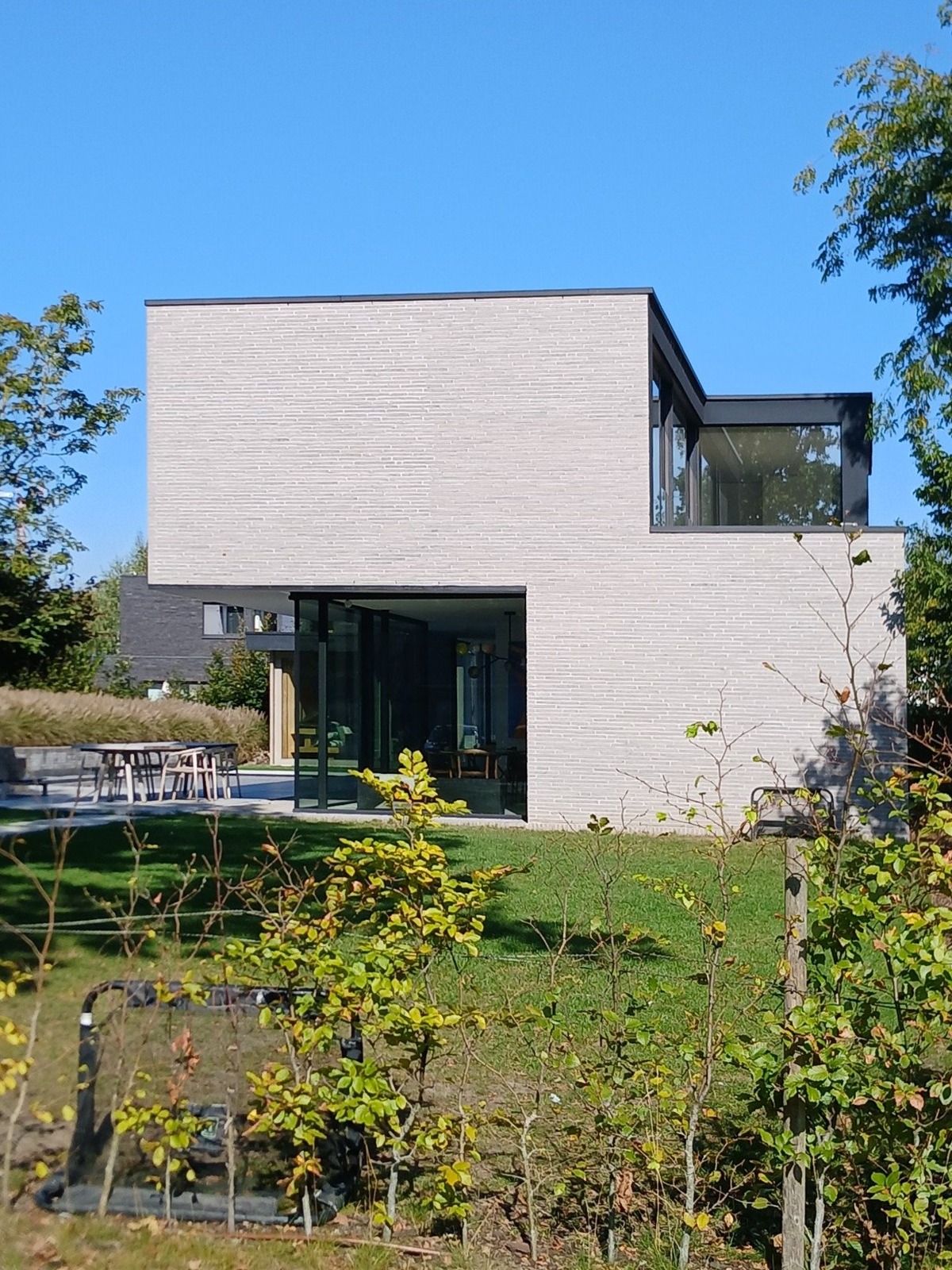 Tuinzijde van de nieuwbouwwoning in Lochristi met een terras voor de glazen wanden
