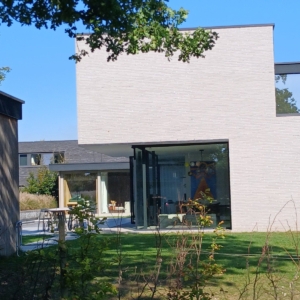 Nieuwbouwwoning in Lochristi met strakke volumes in lichtgrijze baksteen en glazen wanden aan de tuinkant, een project van Bouwwerken Goossens