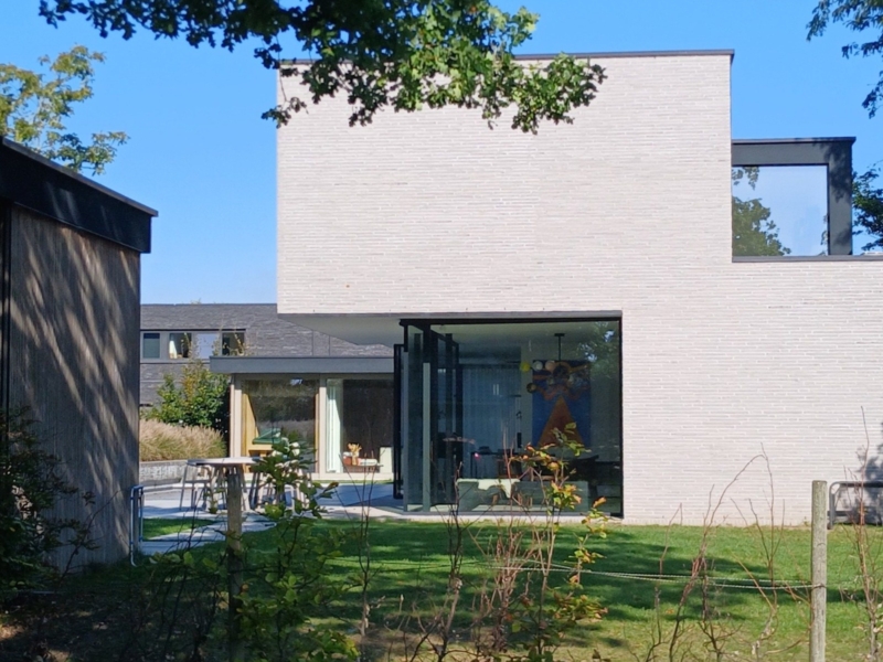 Nieuwbouwwoning in Lochristi met strakke volumes in lichtgrijze baksteen en glazen wanden aan de tuinkant