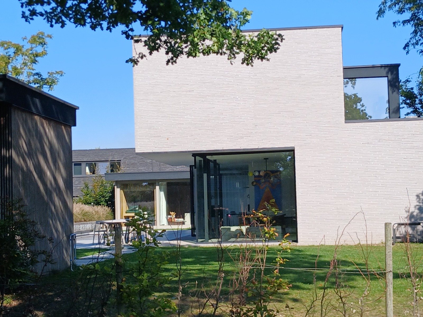 Nieuwbouwwoning in Lochristi met strakke volumes in lichtgrijze baksteen en glazen wanden aan de tuinkant, een project van Bouwwerken Goossens