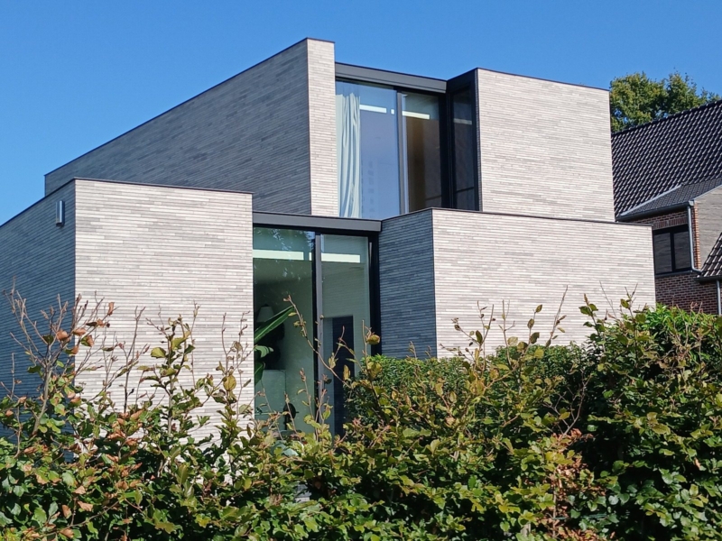 Nieuwbouwwoning in Lokeren uit rechthoekige blokken in lichtgrijze baksteen, met platte daken, achter een beukenhaag, een project van Bouwwerken Goossens