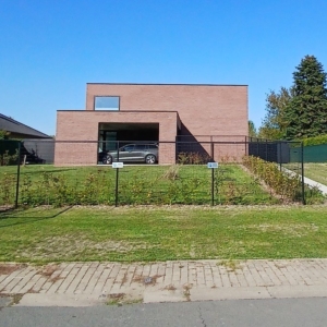 Nieuwbouwwoning in Steenhuize met twee strakke volumes in rode baksteen, een plat dak en een overdekte autostaanplaats, een project van Bouwwerken Goossens