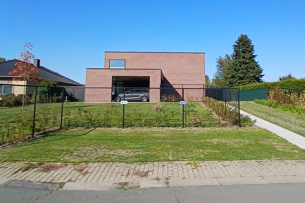 Nieuwbouwwoning in Steenhuize met twee strakke volumes in rode baksteen, een plat dak en een overdekte autostaanplaats, een project van Bouwwerken Goossens
