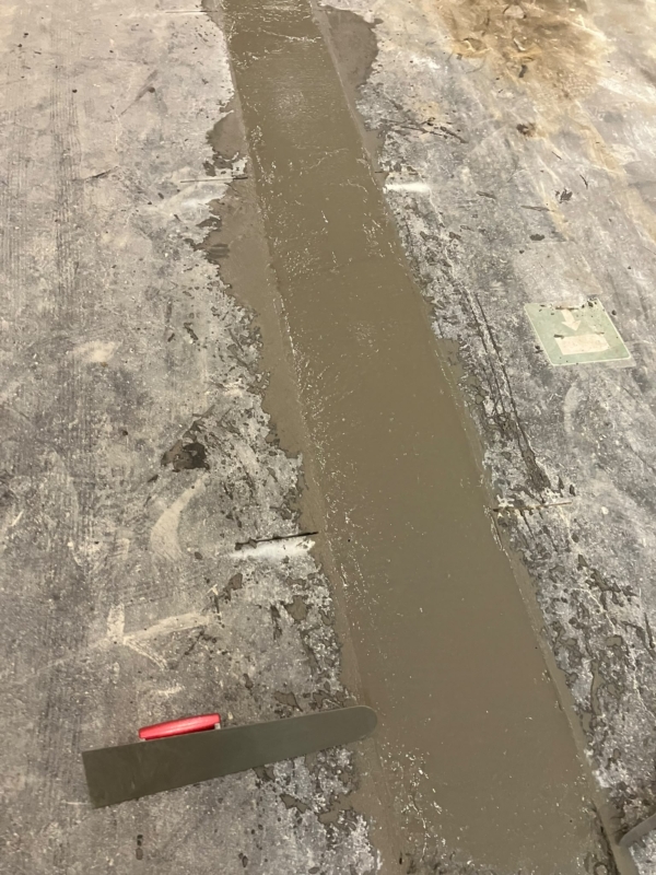 Vers afgewerkte strook beton in de vloer van een bedrijfsruimte met een spaan ernaast, een project van Bouwwerken Goossens
