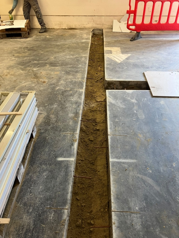 Open sleuf in de betonvloer van een bedrijfsruimte met stalen stekken in de bestaande vloer, een project van Bouwwerken Goossens