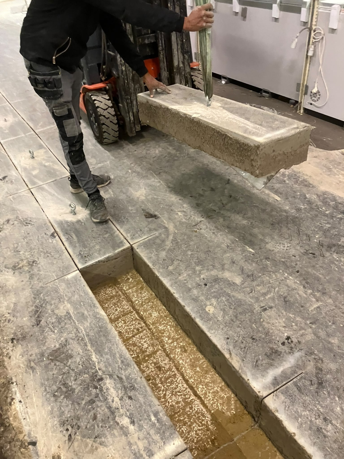 Een uitgezaagde betonplaat gaat met een heftruck en hijsogen in één stuk uit de vloer van een bedrijfsruimte, een project van Bouwwerken Goossens