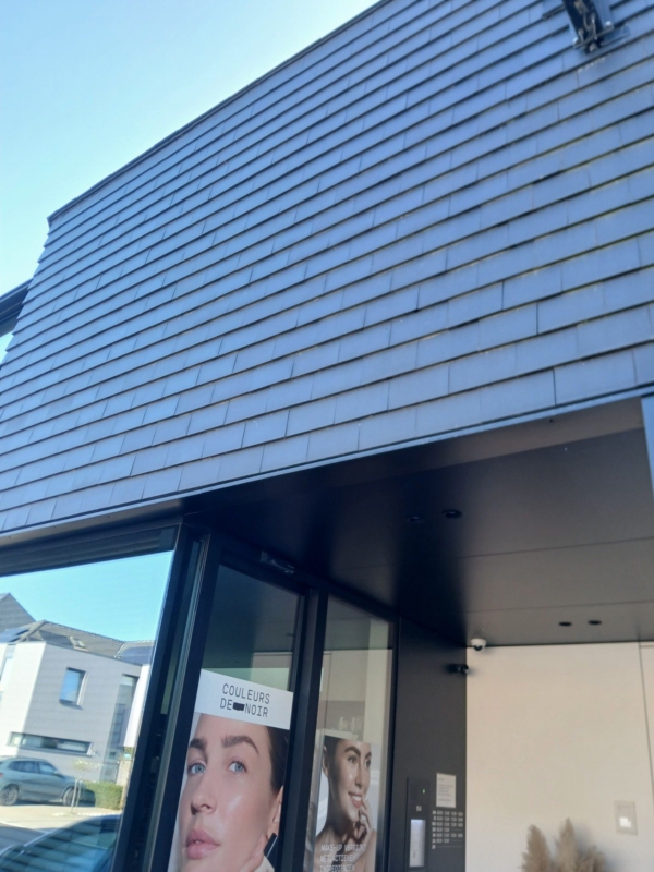 Overdekte doorgang naar de ingang van de apotheek in Bavegem, met glazen deuren en een gevel in donkere leien