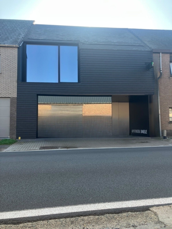 Zwarte voorgevel van de apotheek in Bavegem met gevelbekleding in leien en een groot raam op de verdieping