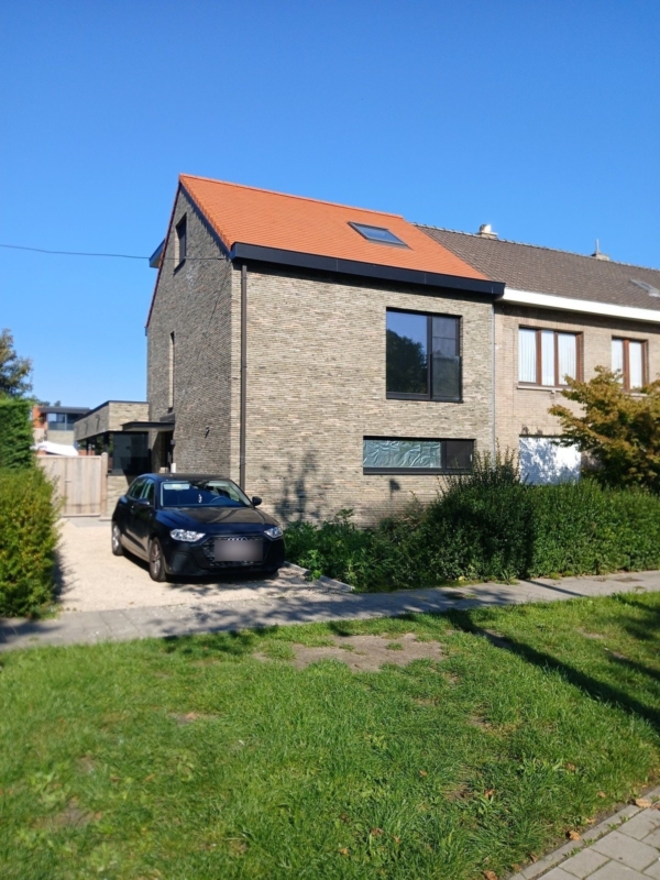 Verbouwde halfopen woning in Gentbrugge met een gevel in grijsbeige baksteen, een oranje pannendak met dakraam en ramen met donkere kaders, een project van Bouwwerken Goossens