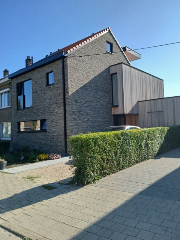 Hoek van de verbouwde woning in Gentbrugge met de houten uitbouw en een haag langs de oprit