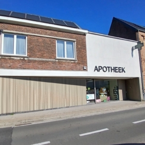 Verbouwde apotheek in een hoekpand in Zottegem met een grote witte gevel met de letters APOTHEEK en houten gevelbekleding op het gelijkvloers, een project van Bouwwerken Goossens